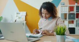 Woman working at a desk with a laptop and notebook.