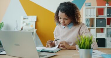 Woman working at a desk with a laptop and notebook.
